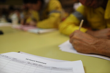 Clear image of job risk assessment booklet placing on the table with defocused construction worker hands written job hazard analysis prior to start working at heights of each job at construction site 