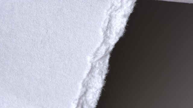 Tearing off textured paper with dark background. Slow motion.