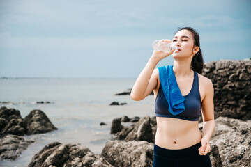 Asian fitness runner body closeup doing warm-up routine on beach before running, stretching leg muscles with standing single knee to chest stretch. Female athlete preparing legs for cardio workout.