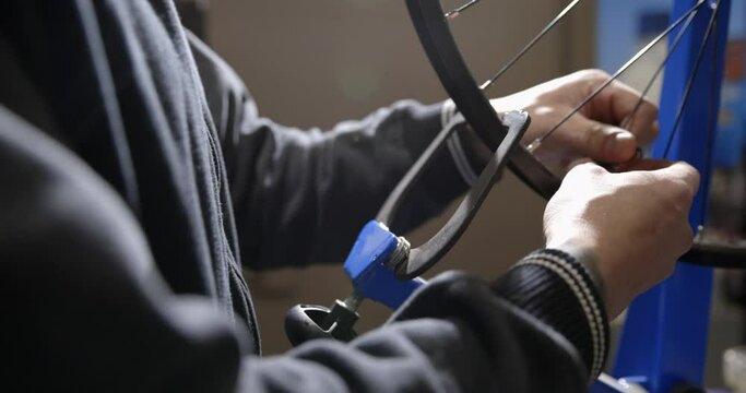 Bicycle mechanic trues wheel on stand - close up on hands