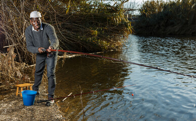 Mature African man standing near river and fishing with rods