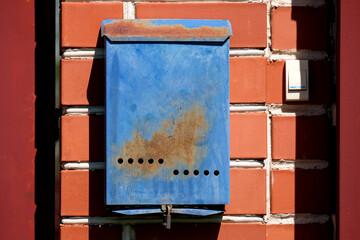 A blue mailbox hangs on a red brick wall outside. Russian post box
