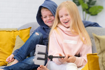 Kids bloggers talking with followers, live streaming, looking to smartphone screen at home. Boy and...