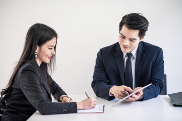 Young asian businessman and businesswoman using touchpad and notebook in office meeting.
