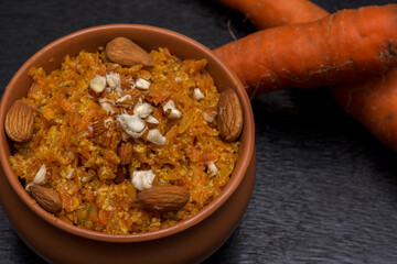 Gajar ka halwa is a carrot based sweet dessert from India. Garnished with Cashew and almond nuts and Served in a bowl over black background.