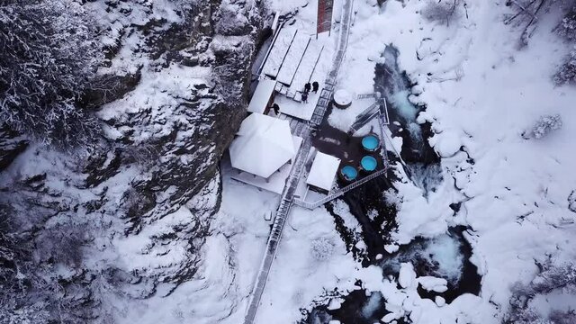 Hot springs in the snowy forest and mountains. Top view from the drone on the white gorge with the river. There are barrels of radon water. There is steam, people are bathing. Almarasan, Almaty.