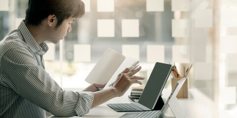 Closeup image of young asian man working on tablet computer and document while sitting at office...