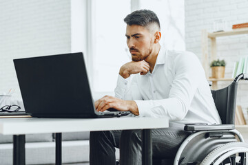 Serious concentrated man in wheelchair using his laptop for work / seeking a job in internet
