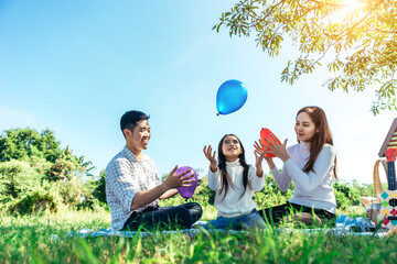 Happy Asian families have a picnic in the garden and happily play with colored balloons together.
