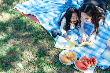 happy Asian family mom and daughter having a picnic in the garden and teaching their daughter to do...