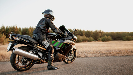 Fototapeta na wymiar Sports bike rider wearing a helmet and leather protective gear on a fast sports bike