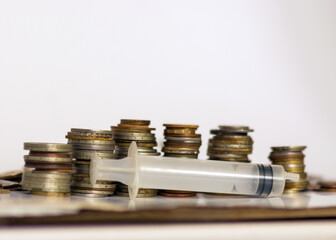 with metal coins of various shapes, countries and values, an empty medical syringe in the foreground