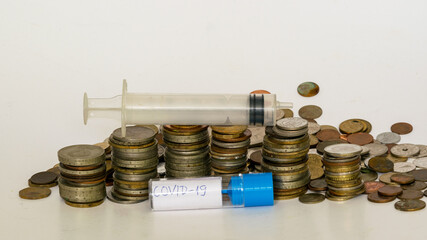 with metal coins of various shapes, countries and values, an empty medical syringe in the foreground