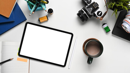 Top view of photographer workplace with digital tablet, camera and accessories on white table.