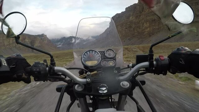 Driving at speed with a motorbike through the Himalayan mountains with grey skies and arid landscapes.