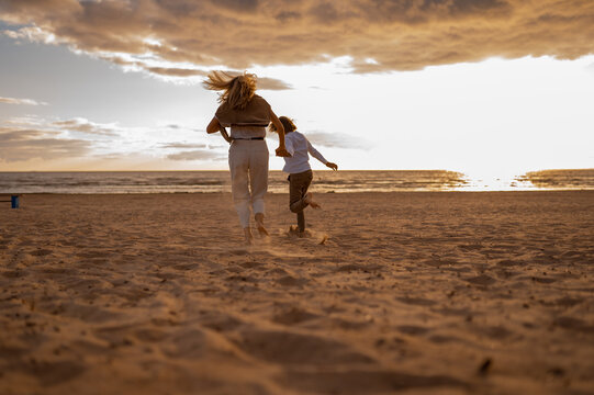 back view of mother and son running together at the beach. Image with selective focus and toning