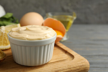 Board with bowl of mayonnaise and ingredients for cooking on wooden background