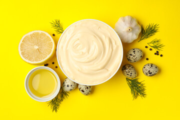Bowl with mayonnaise and ingredients on yellow background