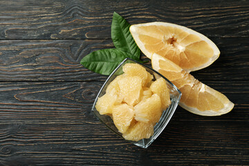 Bowl with pomelo fruit slices and leaves on wooden background