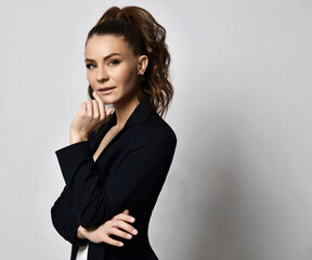 Portrait profile of young businesswoman analyst in official jacket standing side holding hand at her chin over light wall background with copy space. Business, office worker, stylish official look