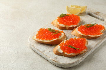 Wooden board with sandwiches with red caviar on white textured background