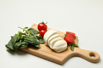 Board with mozzarella cheese, tomato and basil on white background