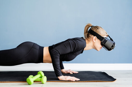 Young blonde woman wearing virtual reality glasses doing push ups at home