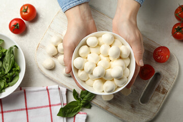 Woman hold bowl with mozzarella cheese over the table with mozzarella and ingredients, top view