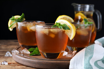 Delicious iced tea on wooden table against black background