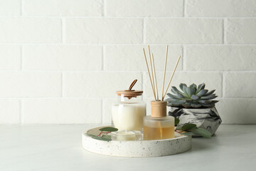 Candles, eucalyptus branches and aromatic reed air freshener on white table near brick wall, space for text. Interior elements