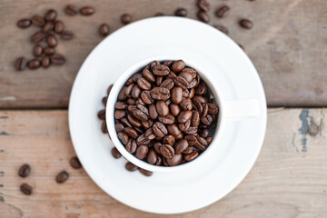 Top view of coffee beans in white cup on wood background