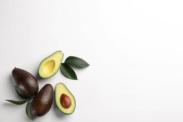 Whole and cut ripe avocadoes with green leaves on white background, top view