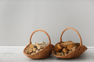 Wicker baskets with firewood near grey wall indoors, space for text