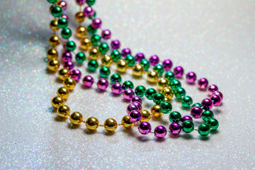 Macro defocused abstract view of traditional three-color Mardi Gras beaded costume jewelry necklaces on a sparkling white glitter texture background