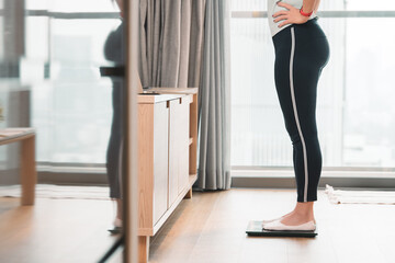 A healthy woman standing on a scale to measuring her weight in the living room after home workout...
