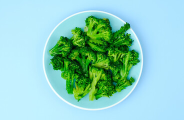 Broccoli isolated on blue plate, on blue background. Top view. Concept of diet food or healthy lifestyle. Vegetarianism and raw food.