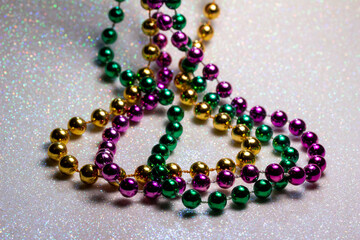 Macro defocused abstract view of traditional three-color Mardi Gras beaded costume jewelry necklaces on a sparkling white glitter texture background