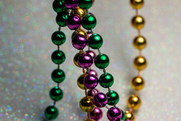Macro defocused abstract view of traditional three-color Mardi Gras beaded costume jewelry necklaces on a sparkling white glitter texture background