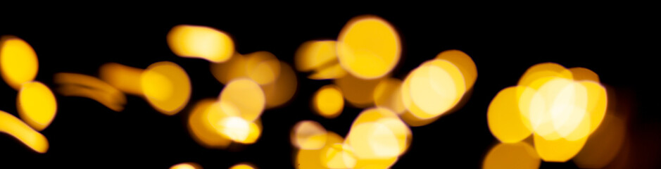 Blurred glowing yellow lights of Christmas garland on black background. Defocus circle bokeh.