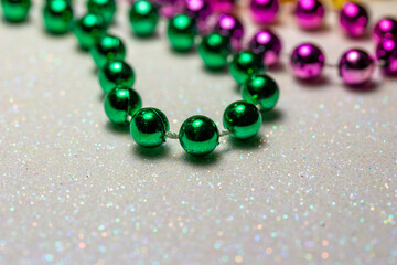 Macro defocused abstract view of traditional three-color Mardi Gras beaded costume jewelry necklaces on a sparkling white glitter texture background