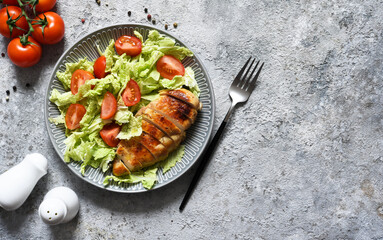 Baked chicken breast and salad with tomatoes on a concrete background. Healthy food, keto diet, paleo diet. Top view with copy space.
