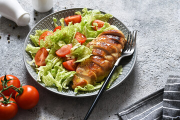 Baked chicken breast and salad with tomatoes on a concrete background. Healthy food, keto diet, paleo diet. Top view with copy space.