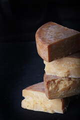 Chunks of hard, perennial cheese are stacked in vertical rows. The concept of still life. Vertical photo on a black background.