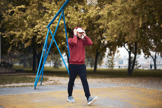 Athletic sporty man training in hoodie sweatshirt in urban city park / basketball court.
