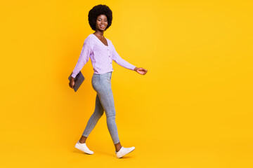 Fototapeta na wymiar Full body profile photo of pretty dark skin person walking arm hold laptop isolated on yellow color background
