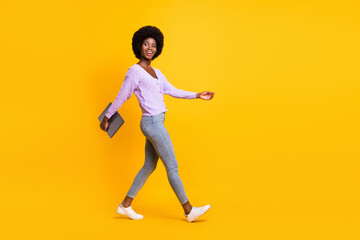 Fototapeta na wymiar Full size profile portrait of cheerful dark skin lady walking hold netbook good mood isolated on yellow color background
