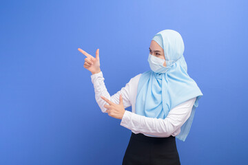 Young muslim woman with hijab wearing a surgical mask over blue background studio.