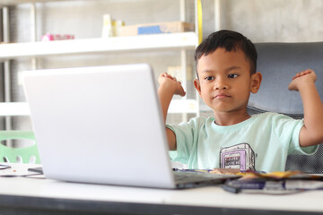 Asian boy kid sitting at table with laptop and preparing to school. Online education concept. Online video call conference class lesson study.
