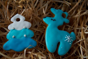 Gingerbread cookies in the shape of a Christmas tree and a deer on wood shavings.