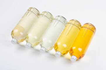 Collection transparent lying bottles with different pale colors liquid, cosmetic product, perfume or drink and silver cap in diadonal row on white background, top view.